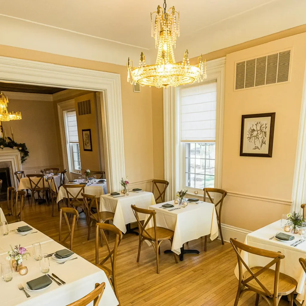 Classic dining room with hardwood floors, white tablecloths, wooden chairs and elegant chandeliers, offering an intimate dining atmosphere.