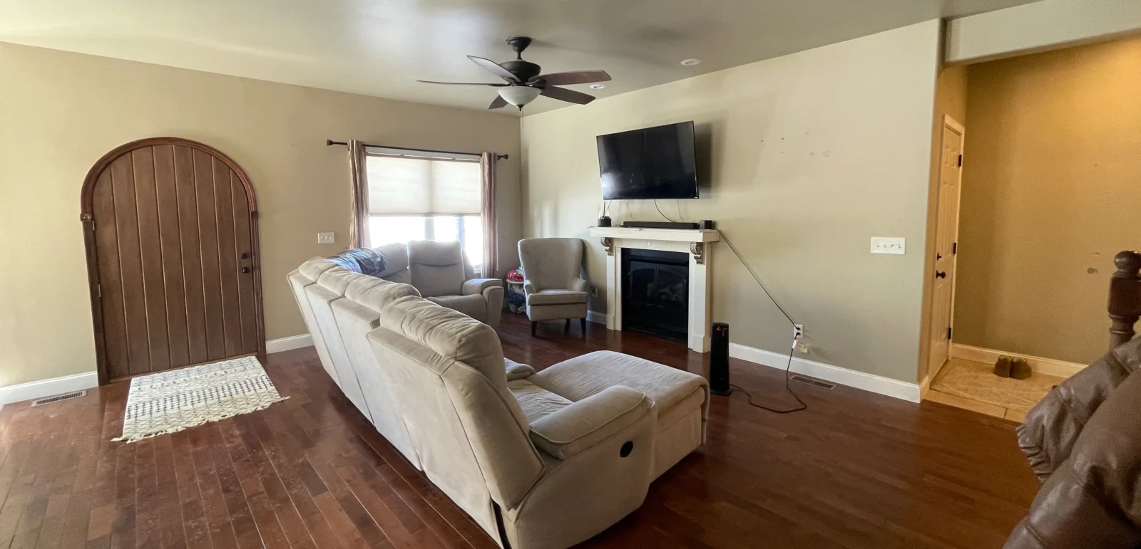 A before image of a living room with beige walls, dark wood floors and a curved wood front door.