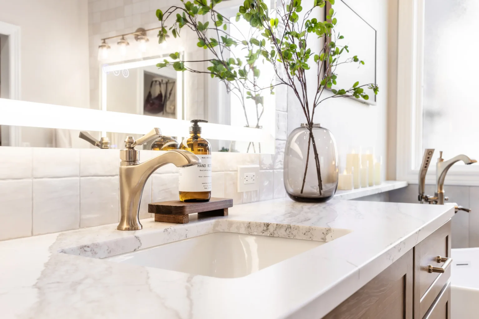 A detailed view of a remodeled bathroom vanity with a quartz countertop and lit mirror.